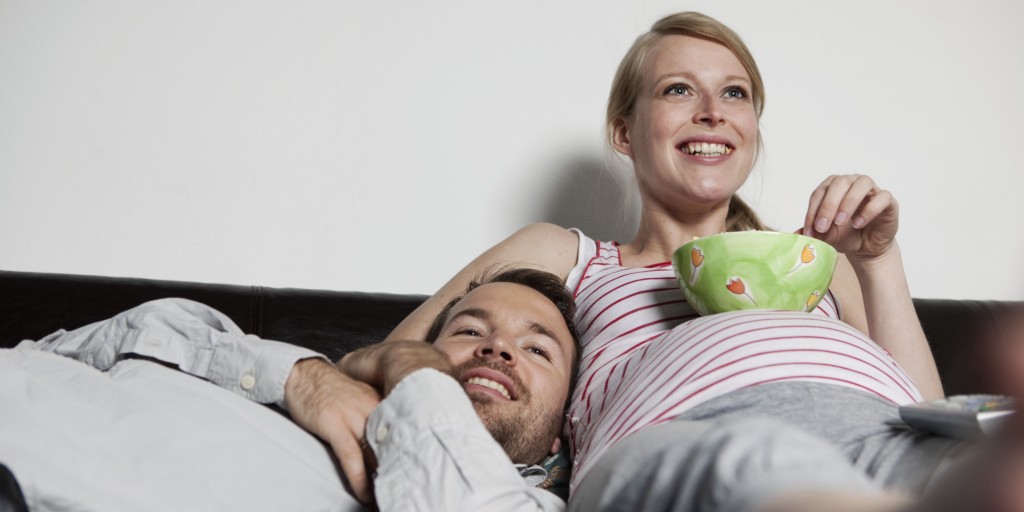 pregnant woman and man on sofa eating popcorn